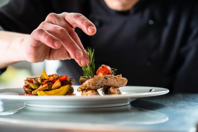 Koch verfeinert und garniert ein Gericht mit Schweinefleisch und Gemüse im Restaurant Gourmetfabrik Schwerin